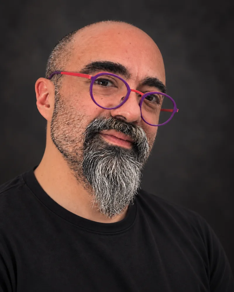 Onur, mor çerçeveli gözlük ve siyah gömlekle pencere yanında oturuyor.